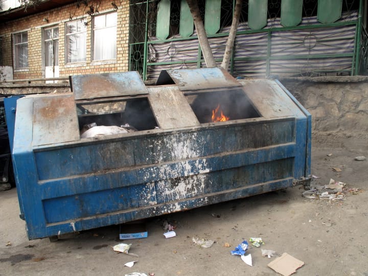 Photo of a large dumpster in a run-down alley; the dumpster is on fire