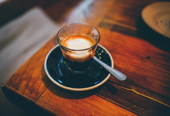 A photo of a proper-looking espresso macchiato sitting on a dark wooden table